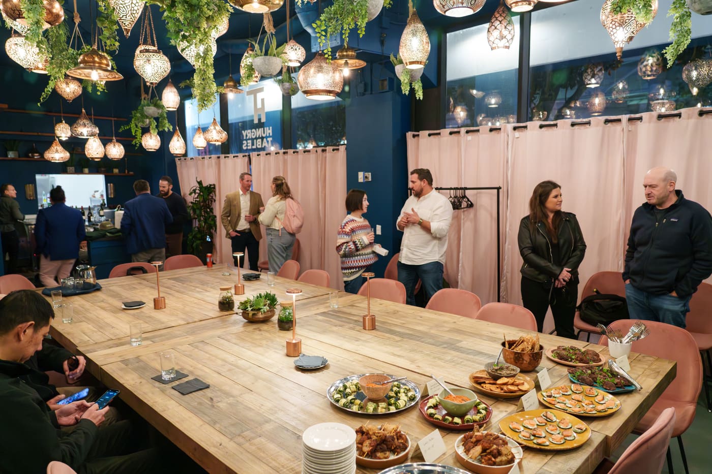 An evening corporate reception: the spread laid down the communal table, guests mingling under lanterns
