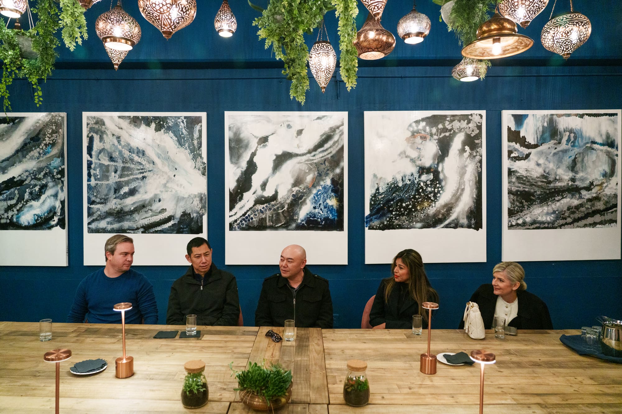 A corporate roundtable in session at the Hungry Tables communal table, beneath the art wall and lanterns