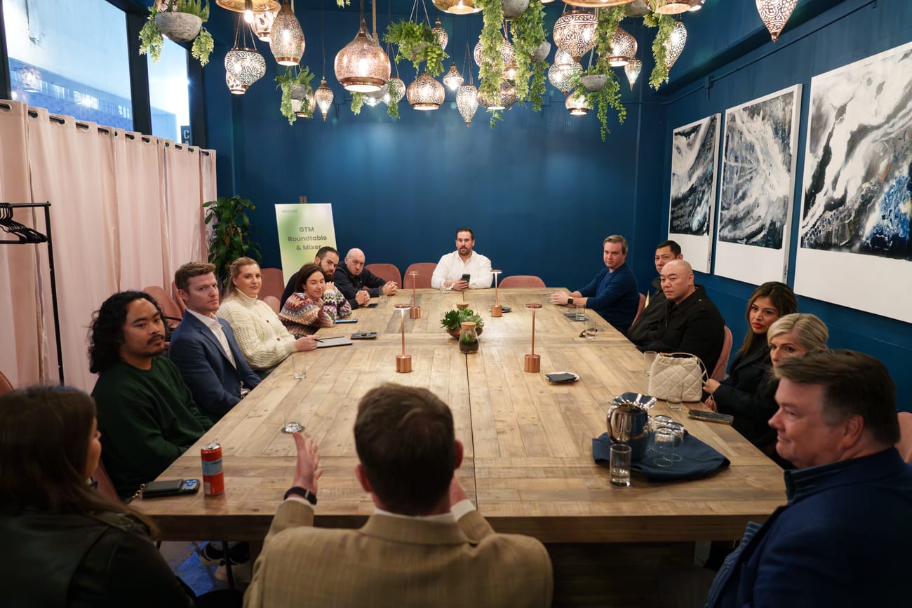 A corporate roundtable from the head of the table: fifteen people seated around it, the speaker presenting at the far end