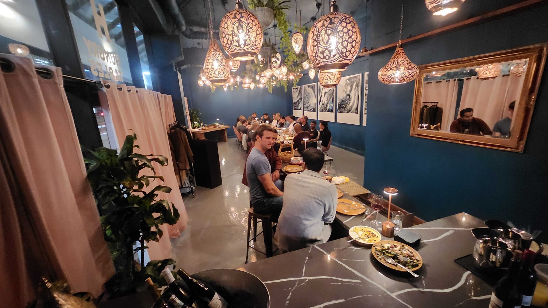The room at night: copper lanterns glowing over full tables and the gold-framed mirror